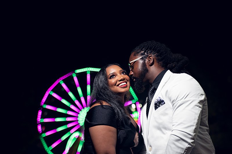 Black man with locs and black woman with long hair and red lipstickin white blazer at nc state fair engagement session