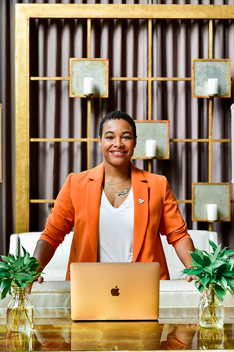Fashionable Black business woman wearing orange blazer and white tee while working on laptop in the lobby of Proximity Hotel, Greensboro NC