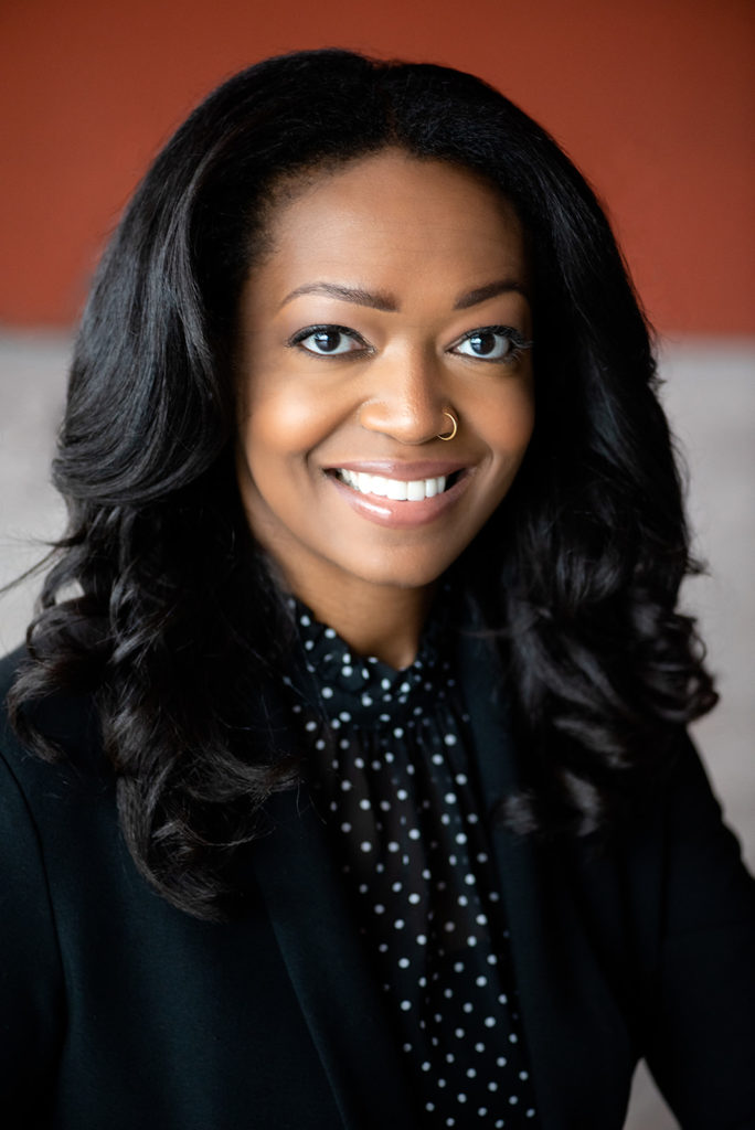 Headshot of caramel complexion black woman with long wavy hair and corporate attire 