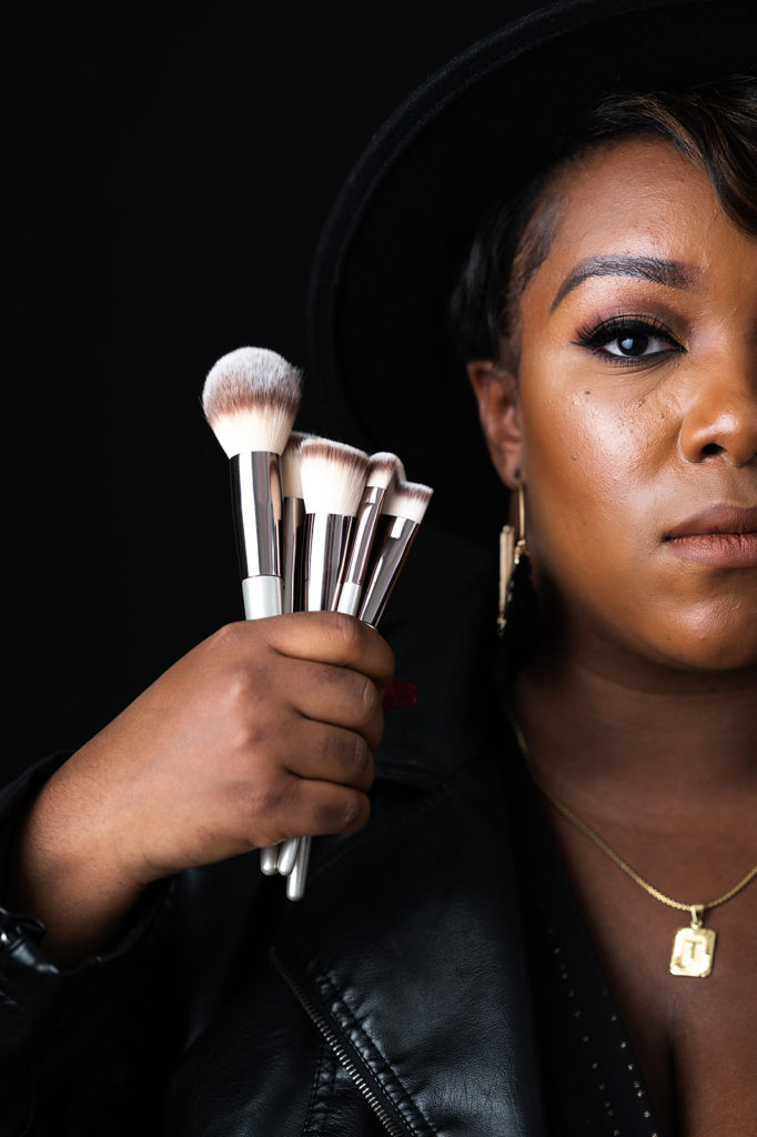 Photograph of Black NC makeup artist holding her brushes against black backdrop Wonderfully Made By Tay NC