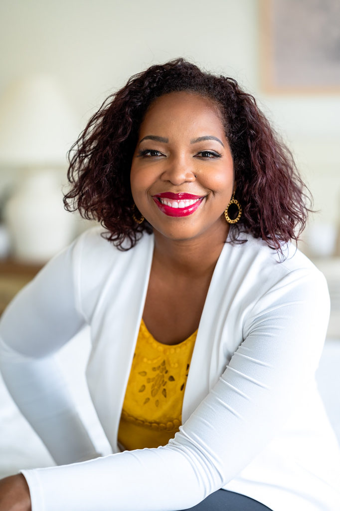 NC Headshot of Black woman with red lipstick, white blazer and yellow blouse