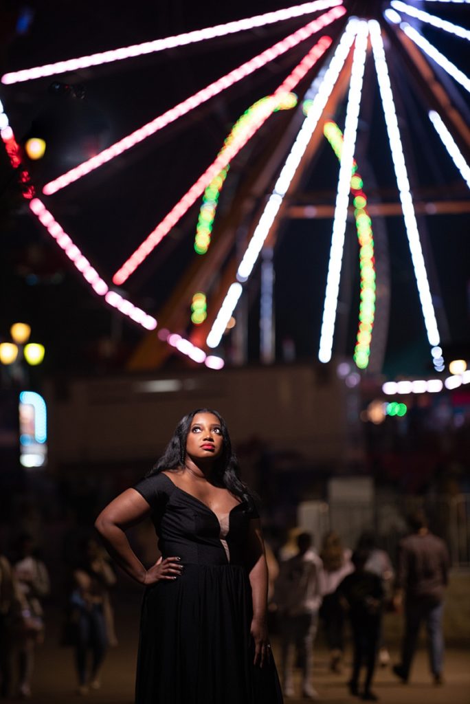 Black woman in black dress in front of ferris wheel at nc state fair engagement session