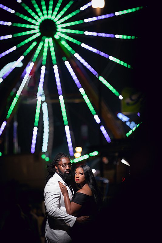 Black couple hugging in front of ferris wheel at nc state fair engagement session
