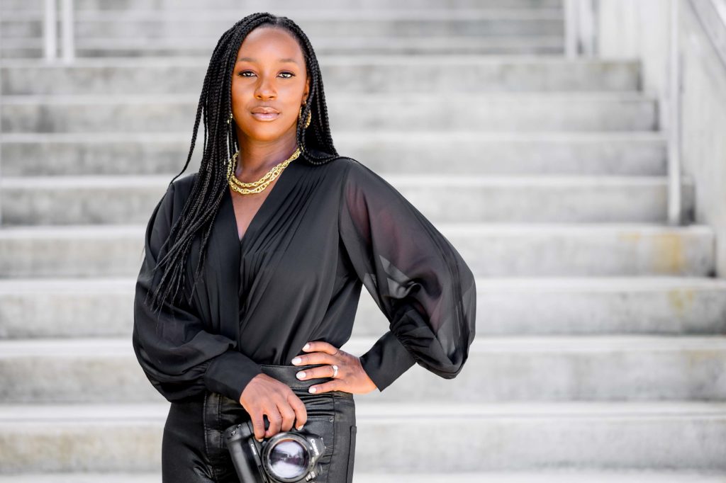 Black woman photographer in braids and black blouse holding nikon camera