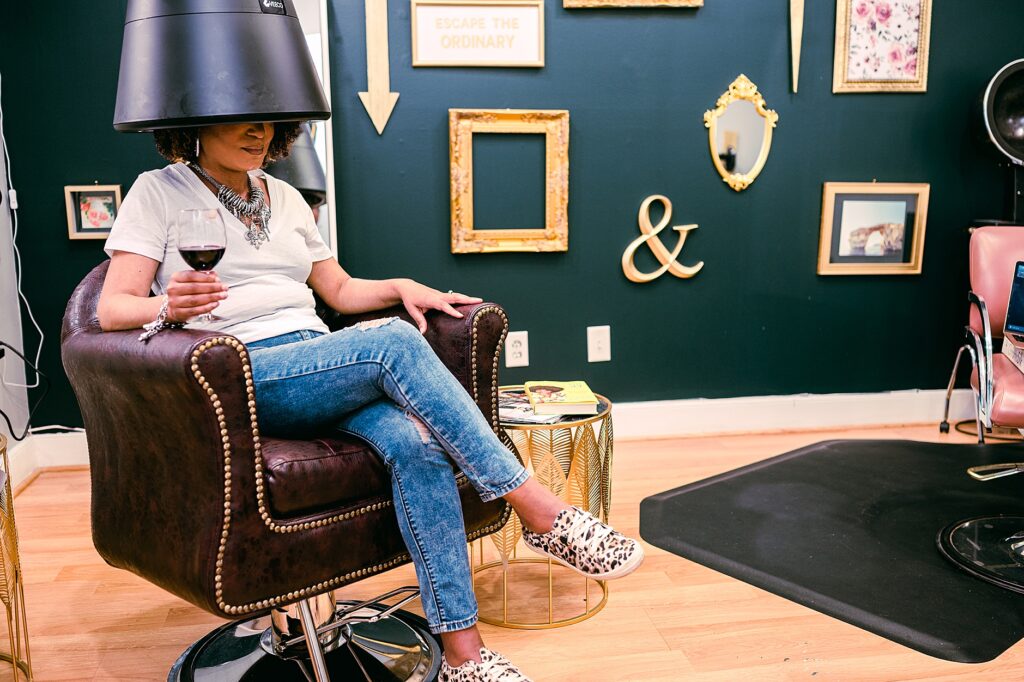 black woman sitting under hair dryer with a glass of wine, Self-Care for Black Women Entrepreneurs